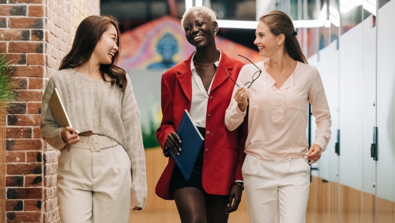 diverse successful businesswomen smiling and walking together in modern workplace