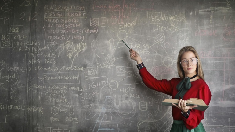 strict female teacher with book pointing at scribbled blackboard