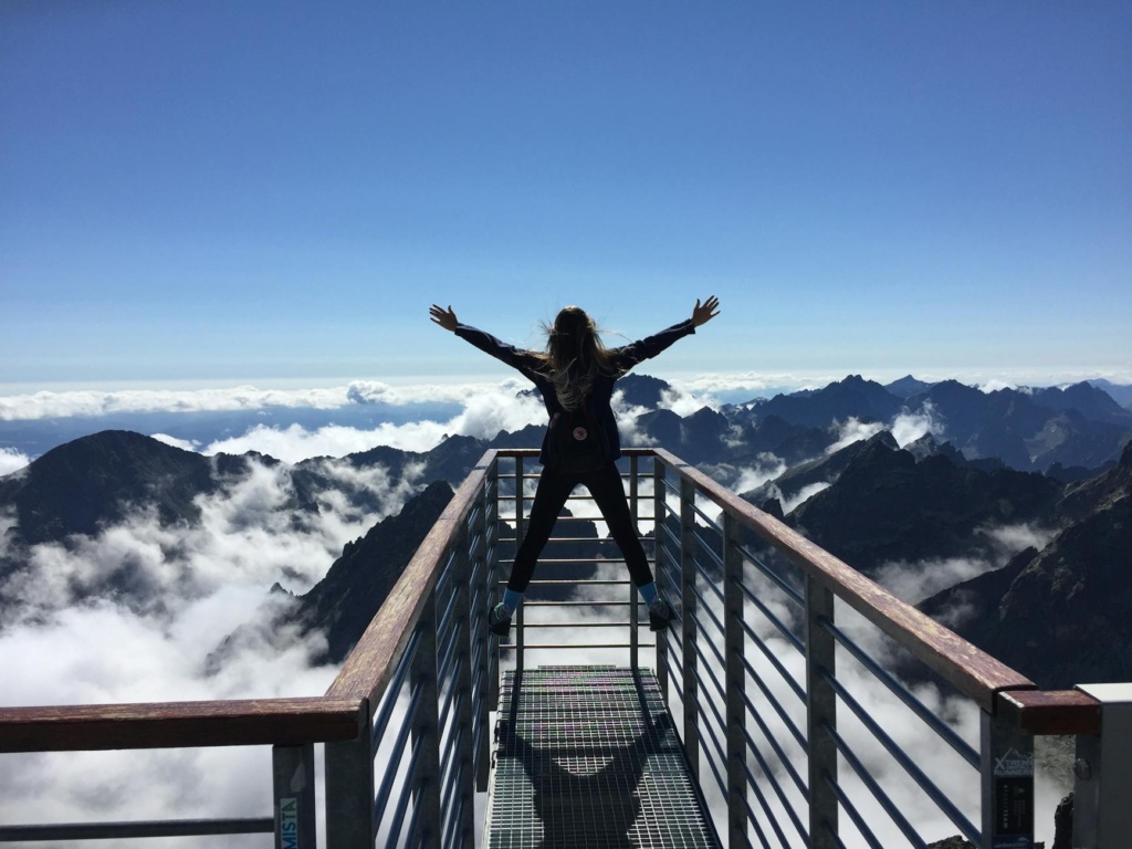 What is success? A person standing on hand rails with arms wide open facing the mountains and clouds after successfully making the trek. 