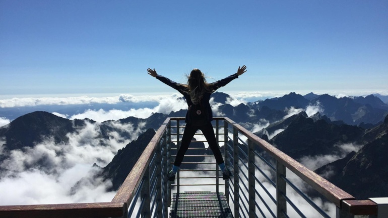 What is success? A person standing on hand rails with arms wide open facing the mountains and clouds after successfully completing the hike!